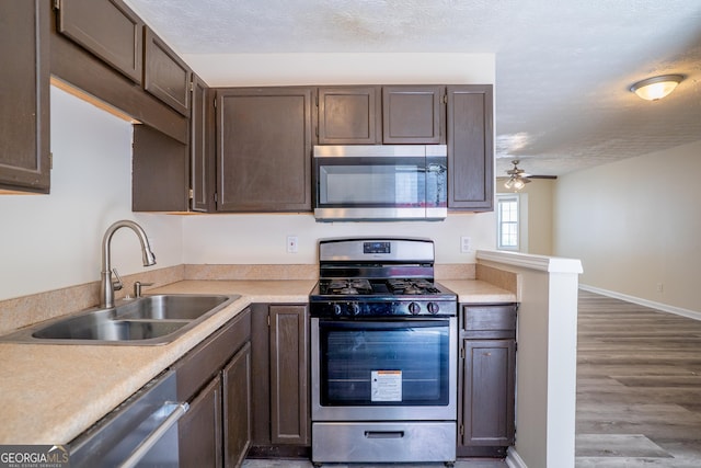 kitchen featuring stainless steel appliances, a sink, light countertops, baseboards, and wood finished floors