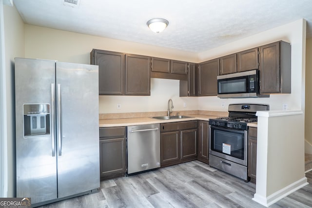 kitchen featuring appliances with stainless steel finishes, a sink, light wood-style flooring, and light countertops