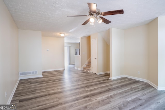 empty room featuring wood finished floors, ceiling fan, stairs, a textured ceiling, and baseboards