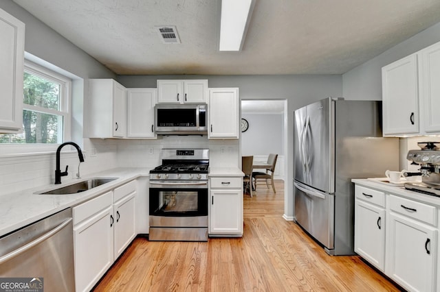 3668 Burel Mill Dr, Buford, GA 30519 - kitchen featuring appliances with stainless steel finishes, a sink, light wood-style floors, white cabinetry, and tasteful backsplash