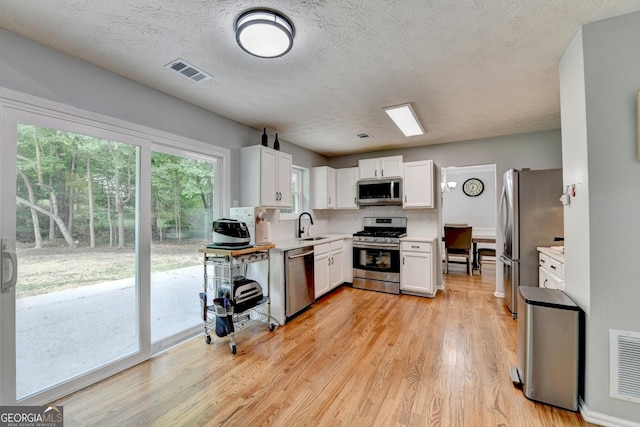 3668 Burel Mill Dr, Buford, GA 30519 - kitchen with stainless steel appliances, a sink, white cabinetry, light countertops, and light wood-style flooring