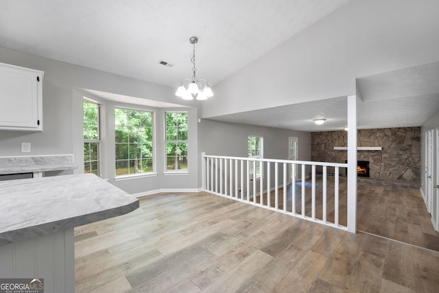 dining area featuring light wood-style floors, vaulted ceiling, healthy amount of natural light, a stone fireplace, and a chandelier