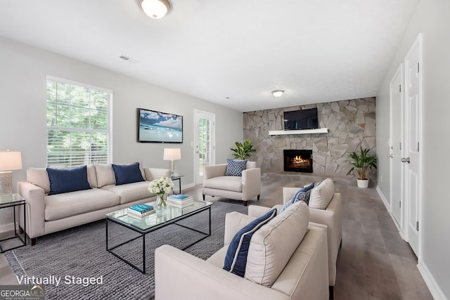 living area with baseboards, a stone fireplace, and wood finished floors