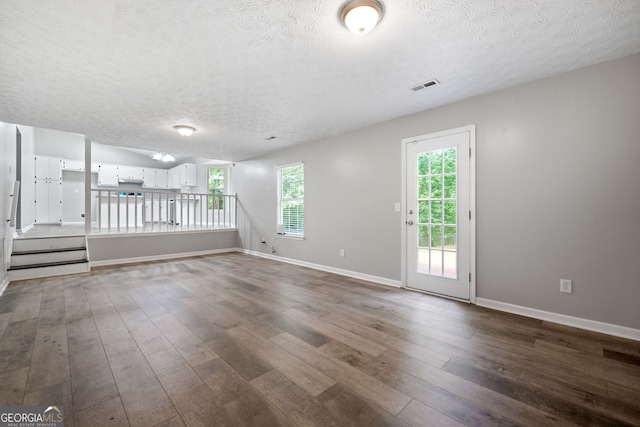unfurnished living room featuring a textured ceiling, dark wood finished floors, healthy amount of natural light, and baseboards