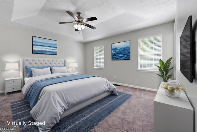 carpeted bedroom with a raised ceiling, baseboards, and a ceiling fan
