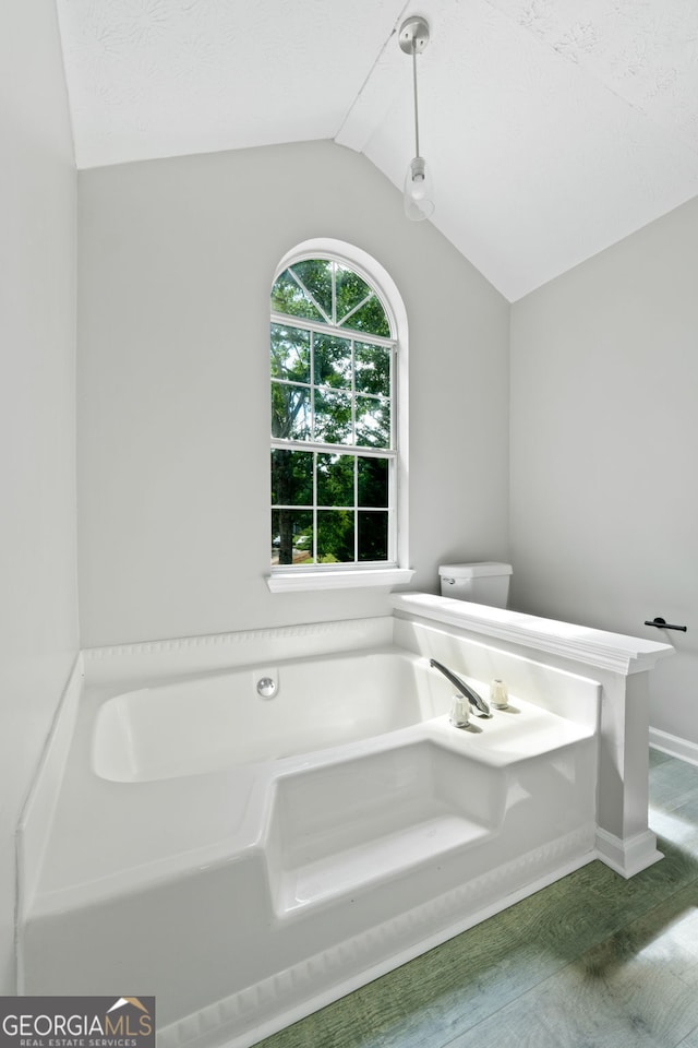 full bath featuring vaulted ceiling, a bath, baseboards, and toilet