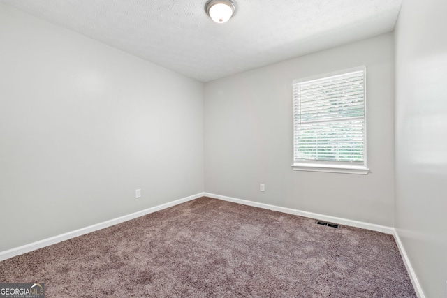 empty room with carpet floors, baseboards, and a textured ceiling