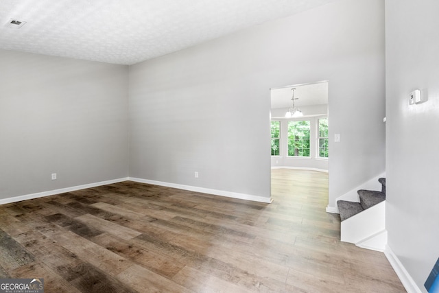 spare room featuring wood finished floors, a chandelier, baseboards, and stairs