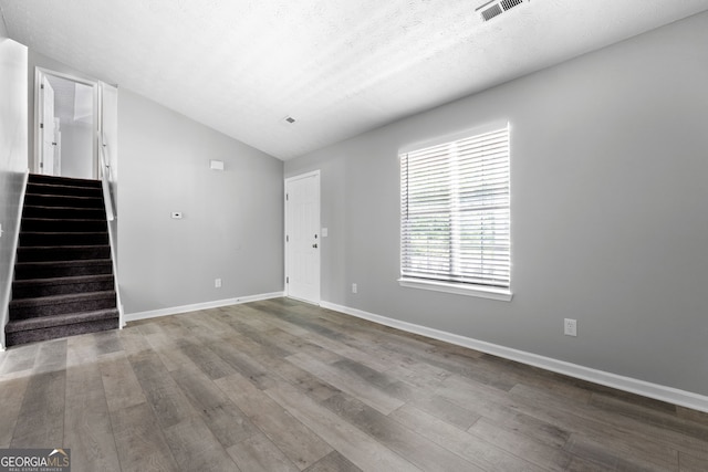 unfurnished living room with vaulted ceiling, stairway, wood finished floors, and baseboards