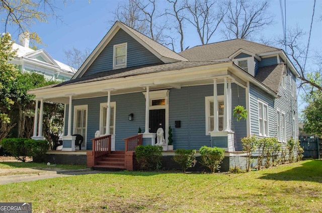 view of front of house with covered porch, a front yard, and roof with shingles