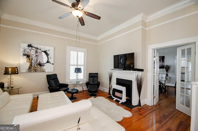 living room with crown molding, hardwood / wood-style floors, ceiling fan, a fireplace with flush hearth, and baseboards