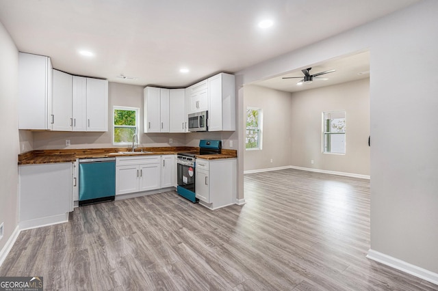kitchen with appliances with stainless steel finishes, a sink, baseboards, a ceiling fan, and light wood-style floors