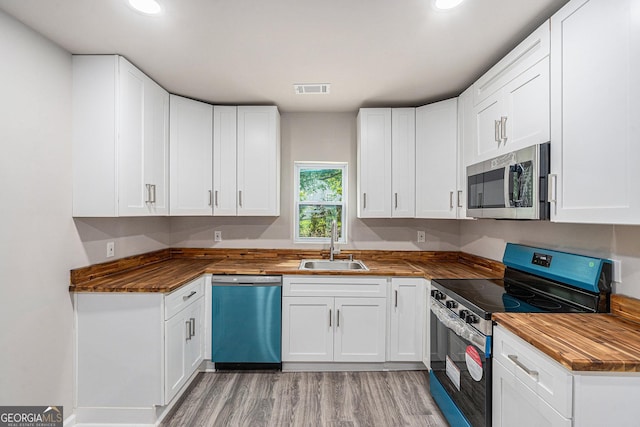 kitchen with stainless steel appliances, butcher block countertops, a sink, light wood-type flooring, and white cabinets