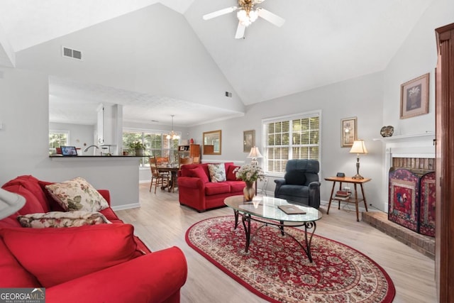 1152 Strath Clyde Way, Mcdonough, GA 30253 - living room with light wood-style flooring, high vaulted ceiling, a ceiling fan, a chandelier, and a brick fireplace