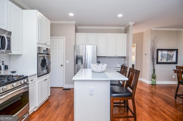 6450 Oak Valley Dr, Cumming, GA 30040 - kitchen with stainless steel appliances, a kitchen breakfast bar, wood finished floors, ornamental molding, and white cabinetry