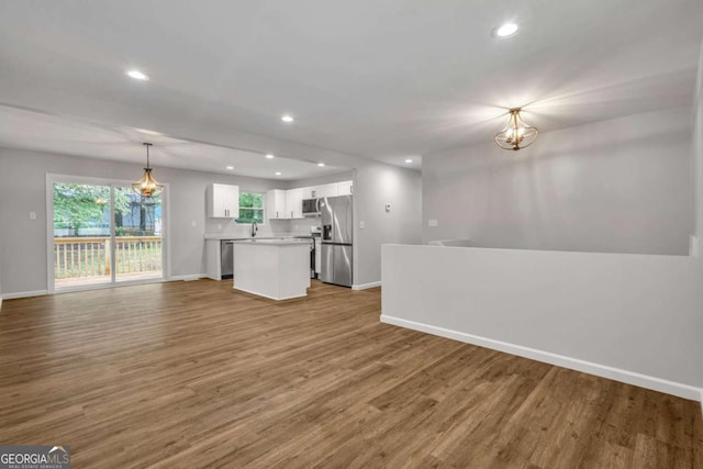 unfurnished living room featuring baseboards, recessed lighting, wood finished floors, a chandelier, and a sink