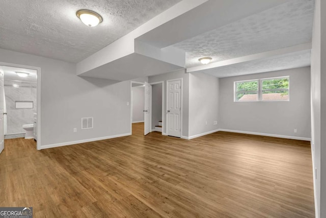 below grade area featuring a textured ceiling, baseboards, and wood finished floors
