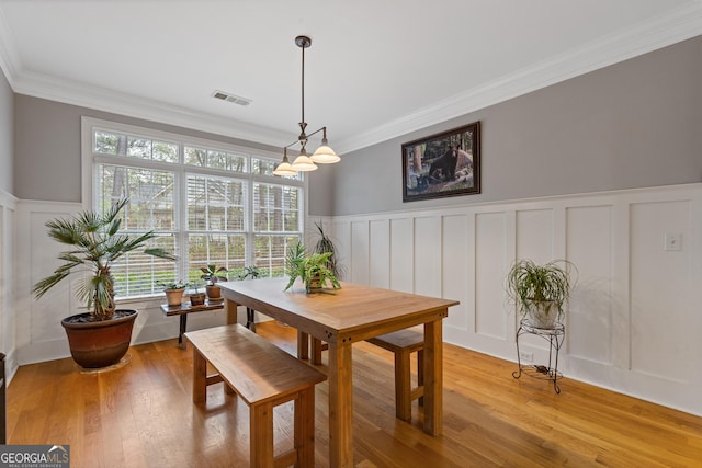 dining room featuring a decorative wall, wainscoting, ornamental molding, and light wood-type flooring