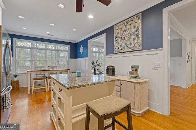 kitchen featuring crown molding, freestanding refrigerator, a decorative wall, a wainscoted wall, and ceiling fan