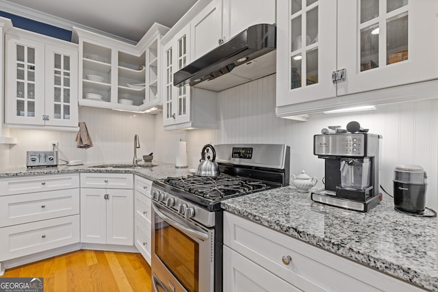 kitchen with stainless steel gas stove, under cabinet range hood, a sink, white cabinets, and light stone countertops