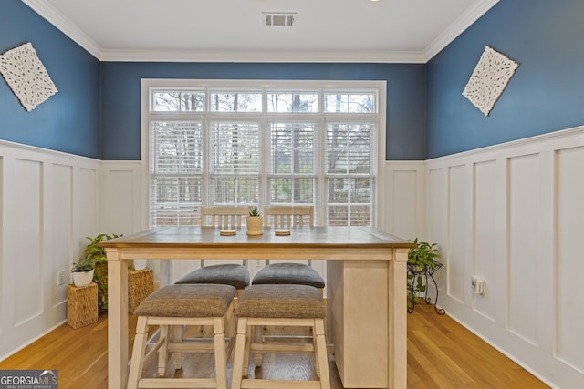 dining room featuring a decorative wall, plenty of natural light, light wood-type flooring, wainscoting, and ornamental molding