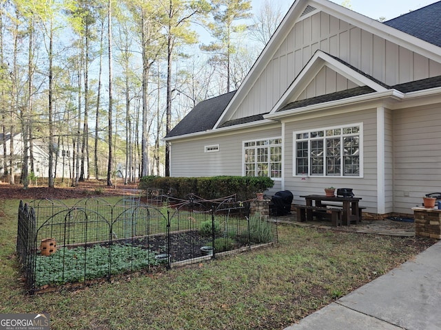 rear view of property with board and batten siding, roof with shingles, and a garden