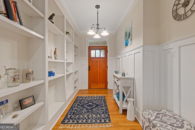 foyer with crown molding, a chandelier, light wood finished floors, wainscoting, and a decorative wall