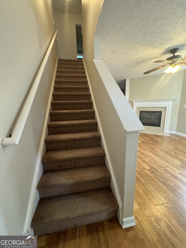 218 Osmanthus Way, Canton, GA 30114 - staircase with wood finished floors, a ceiling fan, a textured ceiling, a fireplace, and baseboards