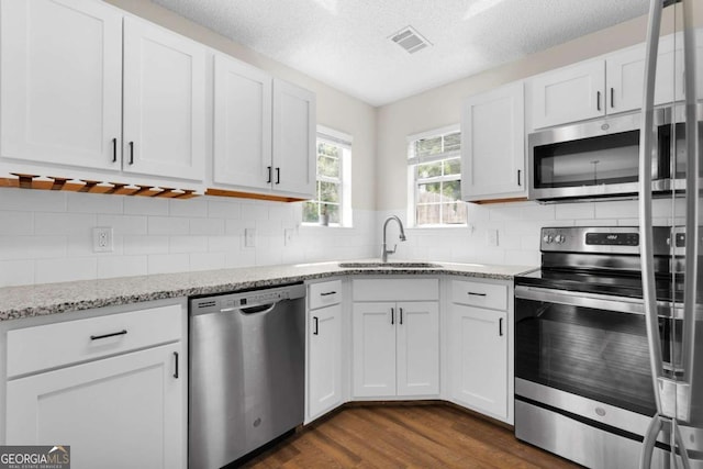 kitchen featuring stainless steel appliances, a sink, dark wood-type flooring, white cabinetry, and a textured ceiling
