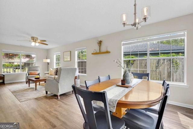 dining area featuring a chandelier, light wood-style flooring, a ceiling fan, and baseboards