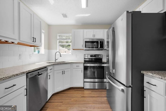 kitchen with appliances with stainless steel finishes, a sink, wood finished floors, white cabinetry, and a textured ceiling