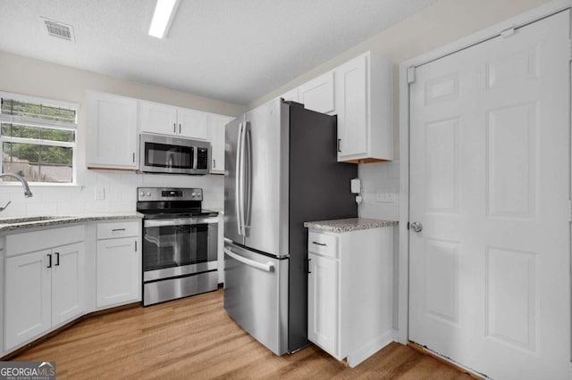 kitchen featuring stainless steel appliances, a sink, light wood-type flooring, and white cabinets