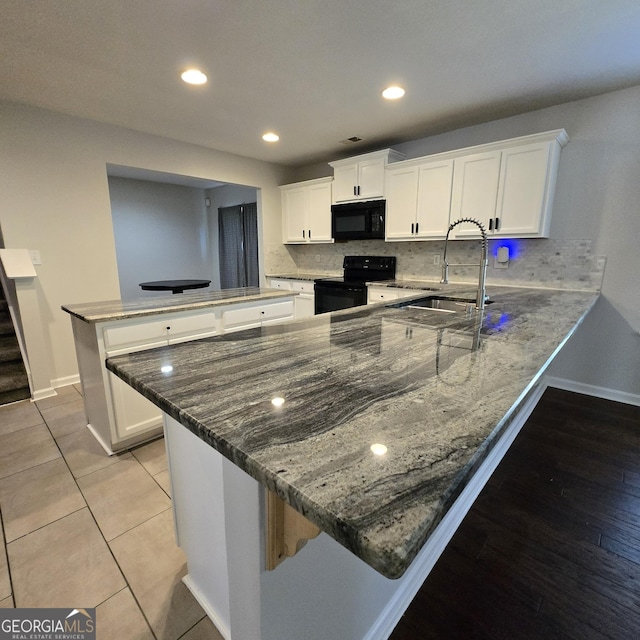 590 Dot Dr, Atlanta, GA 30349 - kitchen with black appliances, a peninsula, baseboards, dark stone counters, and a sink