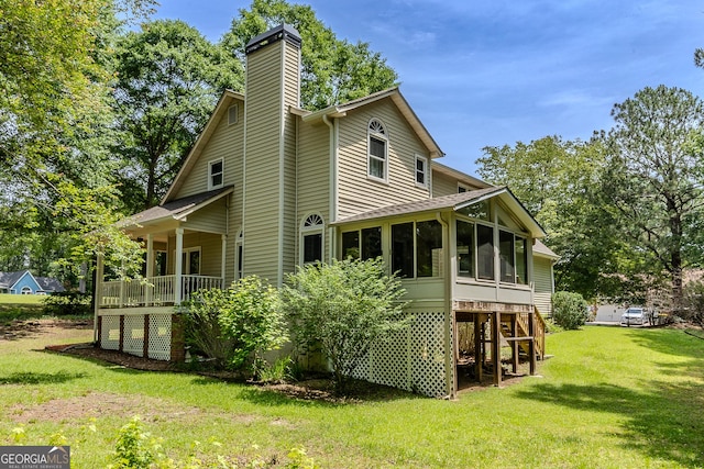 back of house featuring a sunroom, a chimney, and a yard