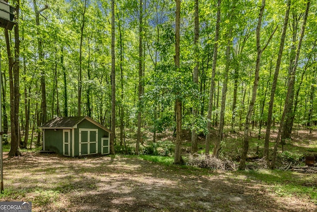 view of yard featuring a storage shed, an outdoor structure, and a forest view