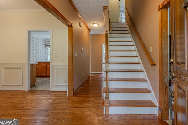 stairway featuring hardwood / wood-style flooring, ornamental molding, a wainscoted wall, a textured ceiling, and a decorative wall