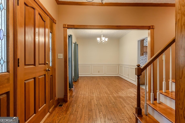 foyer entrance with a chandelier, crown molding, hardwood / wood-style floors, stairs, and wainscoting