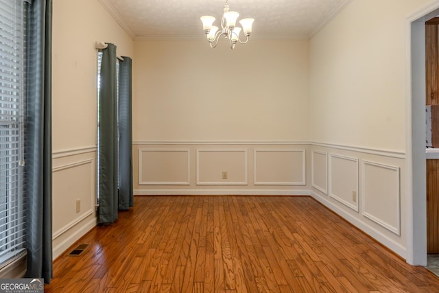 spare room with a chandelier, crown molding, wood finished floors, a wainscoted wall, and a decorative wall