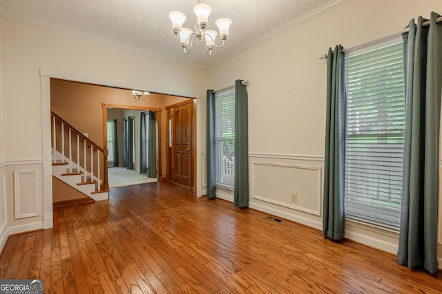 unfurnished room featuring a chandelier, stairs, hardwood / wood-style floors, ornamental molding, and a textured ceiling