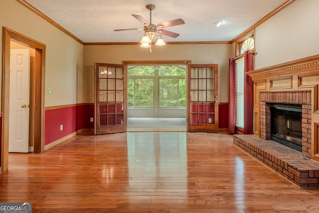 unfurnished living room featuring ornamental molding, wood-type flooring, a ceiling fan, a textured ceiling, and a brick fireplace