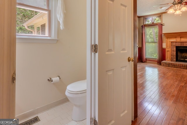 bathroom with toilet, ceiling fan, a fireplace, baseboards, and wood finished floors