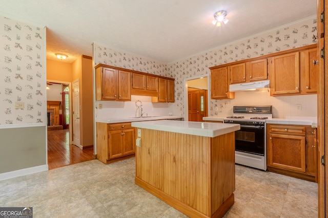 kitchen with gas range, wallpapered walls, under cabinet range hood, tile countertops, and a center island