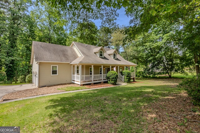 view of front of property featuring covered porch, a front lawn, driveway, a shingled roof, and view of wooded area