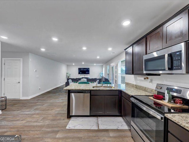 kitchen featuring stainless steel appliances, a peninsula, dark brown cabinetry, open floor plan, and a sink