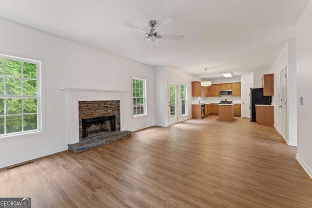 unfurnished living room featuring plenty of natural light, light wood-type flooring, baseboards, and ceiling fan
