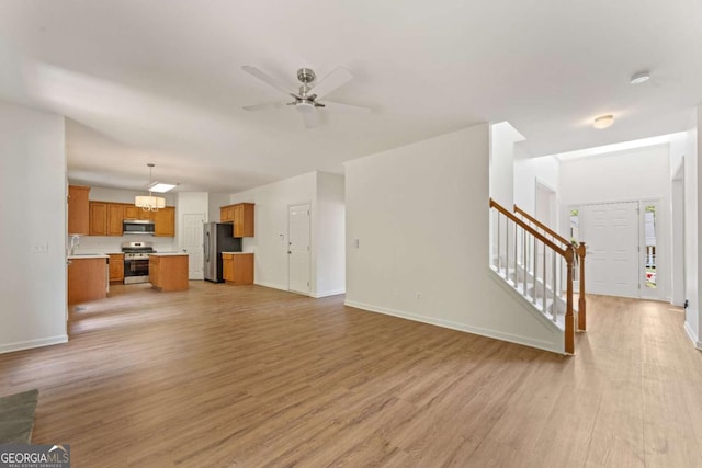 unfurnished living room with stairway, light wood-style flooring, baseboards, a ceiling fan, and a sink