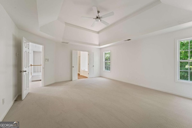 unfurnished bedroom with light carpet, a raised ceiling, and multiple windows