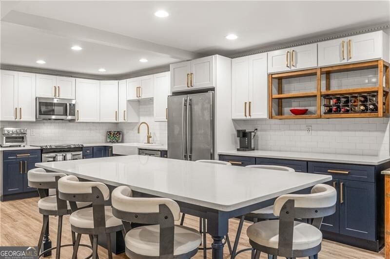 1105 Clairemont Ave Unit O, Decatur, GA 30030 - kitchen with appliances with stainless steel finishes, blue cabinetry, a sink, backsplash, and light wood-style floors
