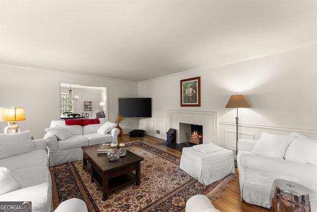living area with wood finished floors, ornamental molding, a chandelier, a lit fireplace, and a decorative wall