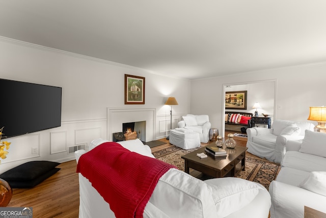 living room with crown molding, wood finished floors, a lit fireplace, a wainscoted wall, and a decorative wall
